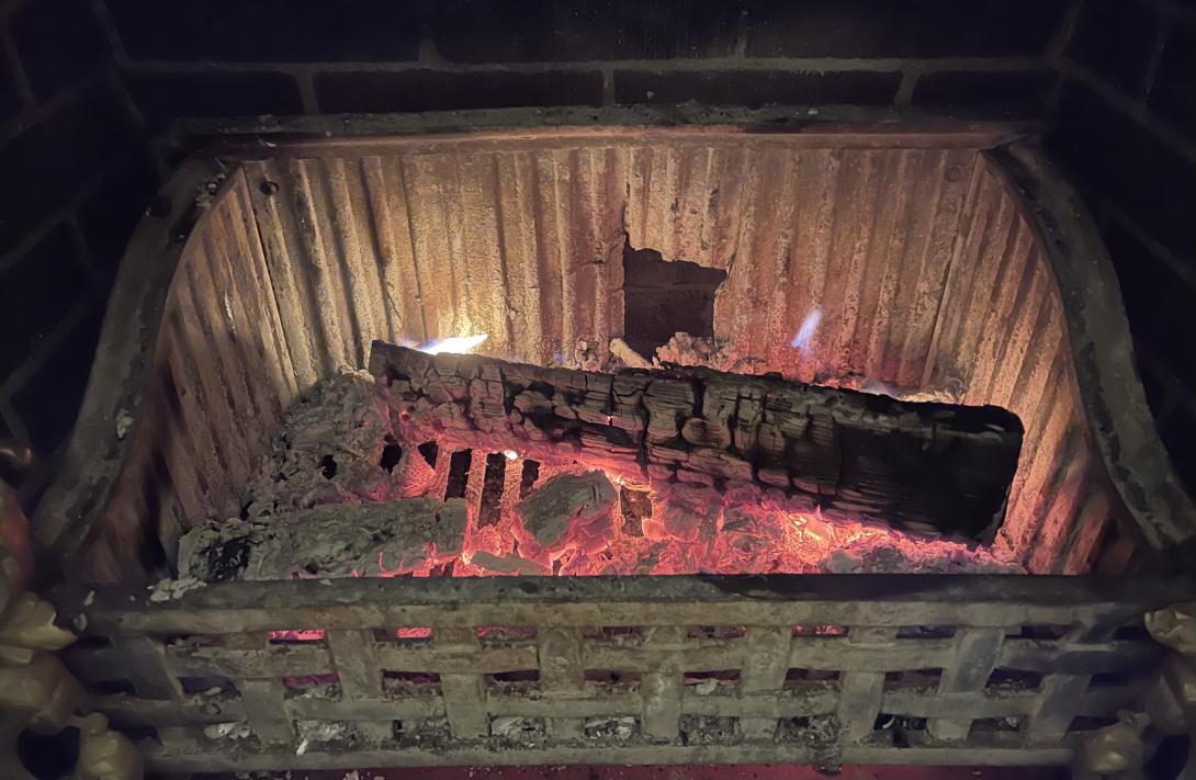 Fireplace with smouldering embers in a steel fire grate. Several logs are visible.