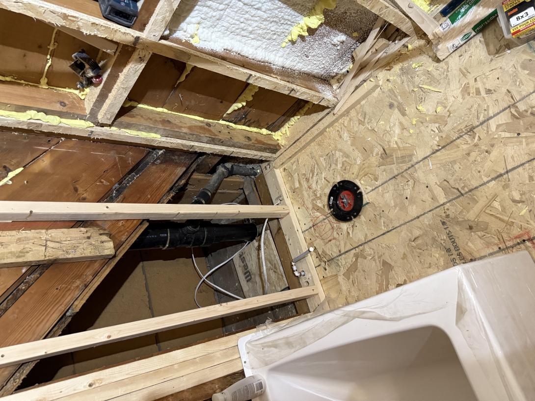 Mid construction. 2024 Photo of a bathroom under construction. The new bathtub is visible and so is the open stud wall and toilet flange in the wooden floor.